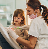 dentist showing a young girl how to brush her teeth